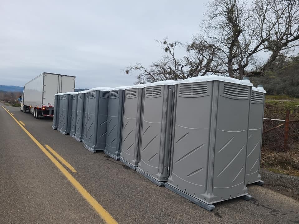 Gray portable toilets lined up beside a road, with a semi-truck in the background.