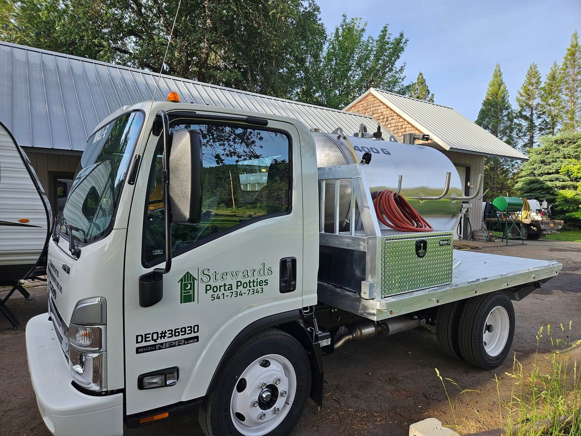 White water truck with a silver tank parked outdoors near a building and trees.