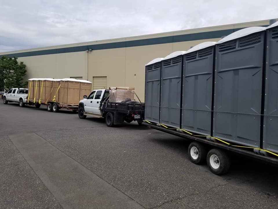 Two trucks with trailers carrying portable toilets parked outside a building.