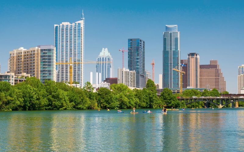 A city skyline with a lake in the foreground and a bridge in the background.