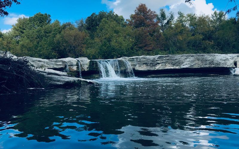 There is a waterfall in the middle of a lake surrounded by trees.
