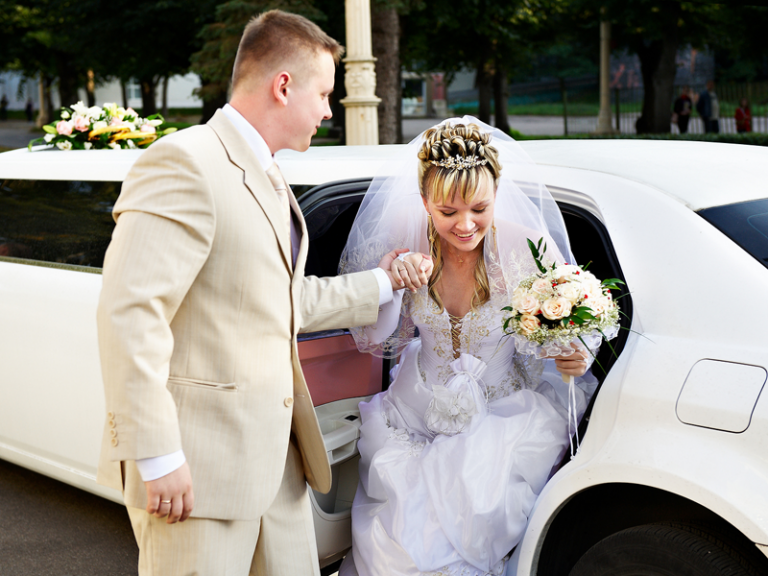 A bride and groom are getting out of a white limousine.