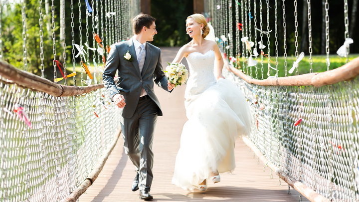 A bride and groom are walking across a bridge holding hands.