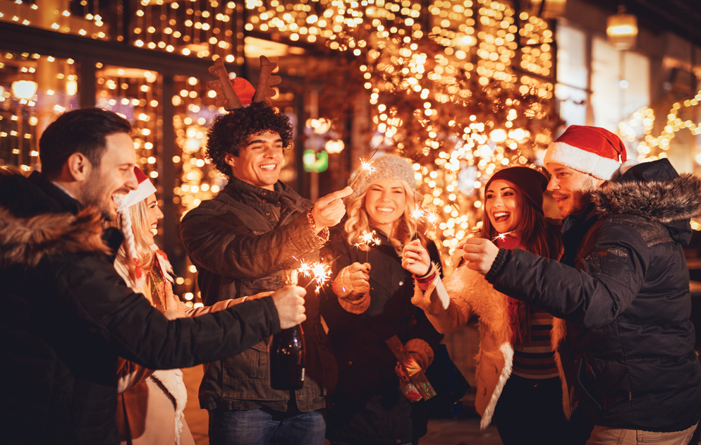 A group of people are holding sparklers in front of a christmas tree.