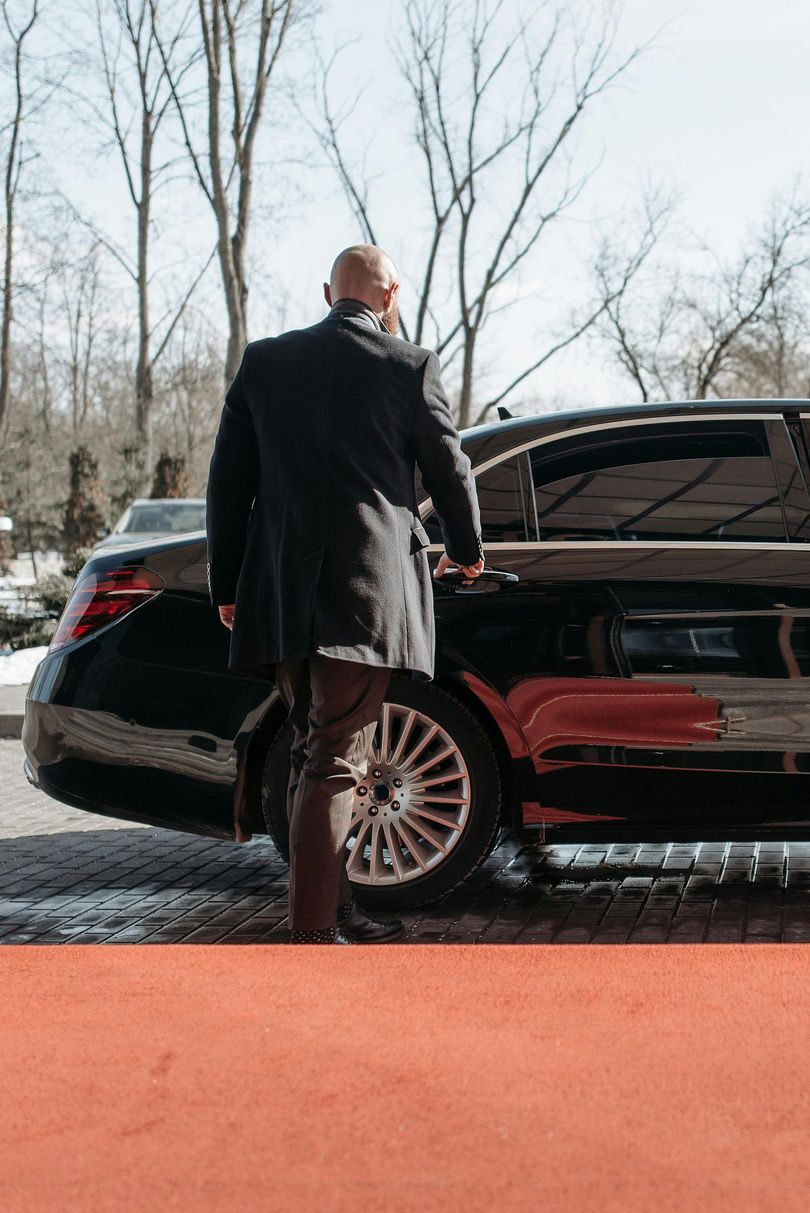 A man in a black coat is standing next to a black car.