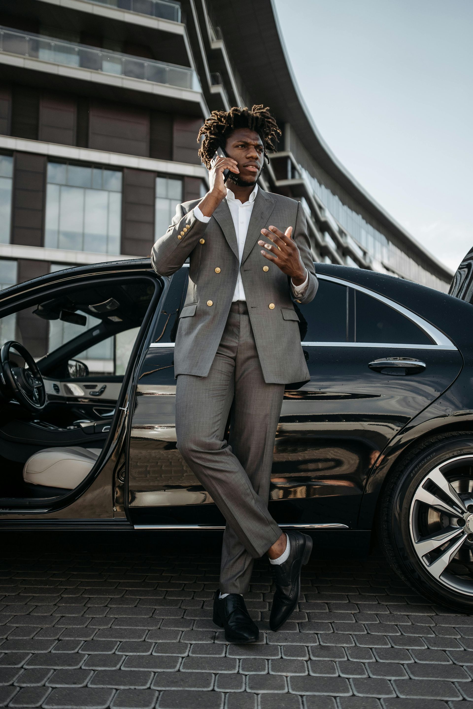 A man in a suit is standing next to a car talking on a cell phone.
