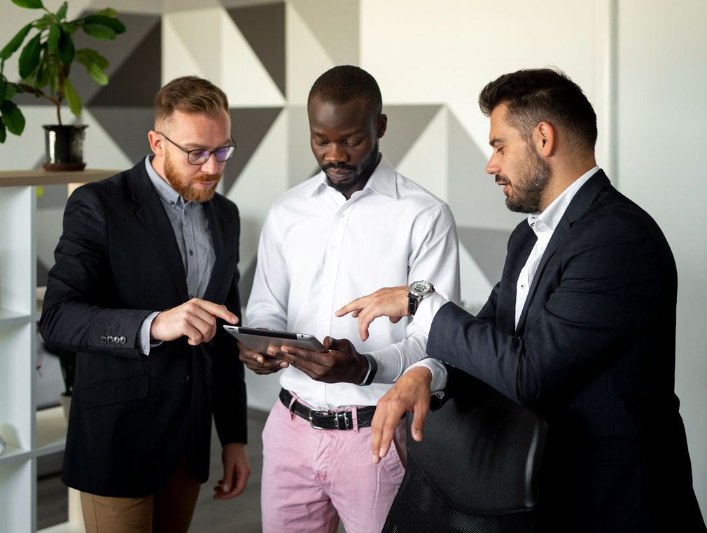 A group of men are standing around looking at a tablet.