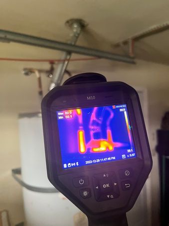 Thermal camera showing heat emanating from a water heater and pipes, orange/yellow indicating the warmest areas.