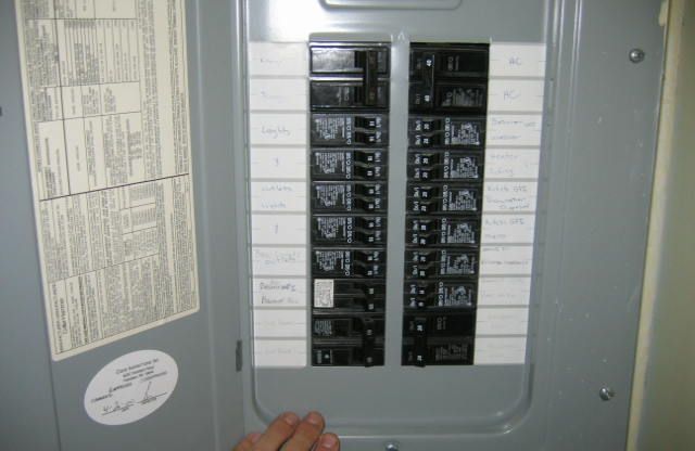 Electrical breaker panel with breakers in the on position. Hand near the panel.