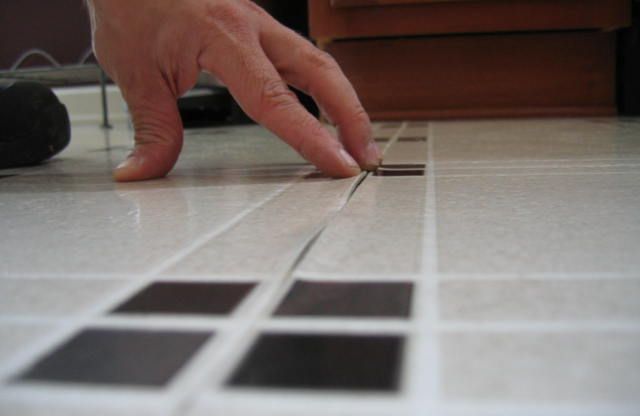 Hand pointing at cracked tile flooring with black and white squares.