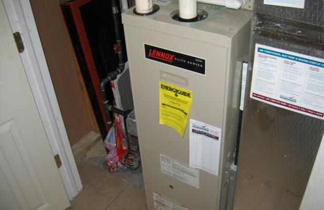 Tan Lennox furnace with yellow energy guide sticker in a basement setting.