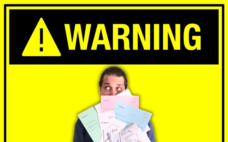A man covering his face with papers under a warning sign about Debt Addiction and How to Overcome It