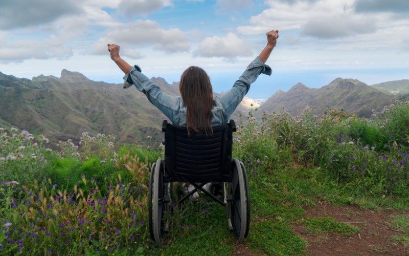 A woman in a wheelchair with her arms in the air symbolizes Debt Forgiveness for the Disabled.
