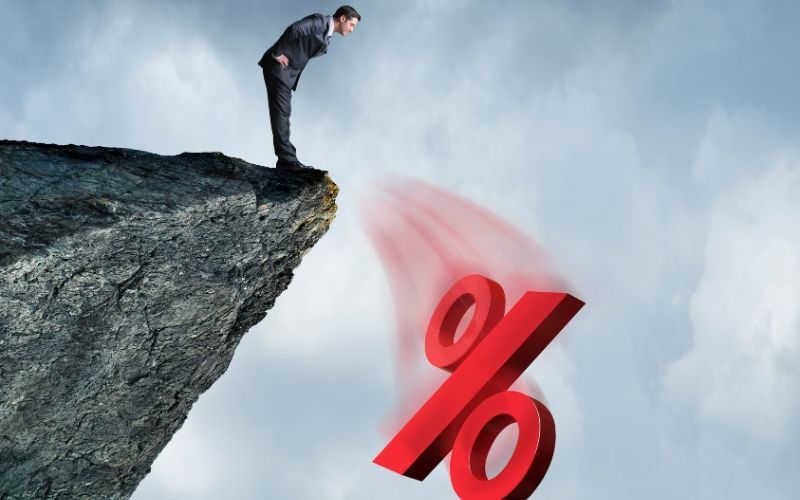 A man is standing on a cliff looking at a red percent sign emphasizing Credit Card Interest.