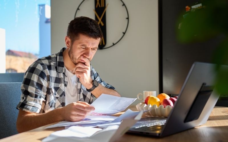 Man looking worried while reviewing bank statements and paperwork at home