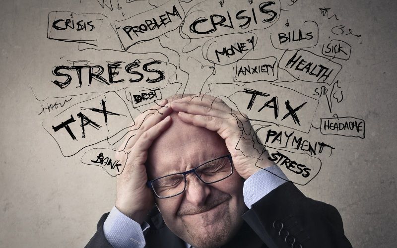 Distressed man holding head amid bills, symbolizing debt stress and need for relief.