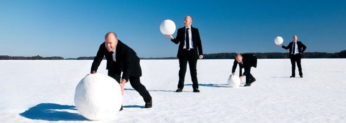 four businessmen in suits rolling increasingly larger snowballs across a snow-covered field, symbolizing the accumulation of payments to clear debts which is known as a Debt Snowball Method