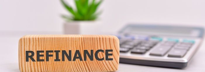 A wooden sign with the word refinance written on it is sitting next to a calculator emphasizing The Pros, Cons, and Key Questions to Consider.