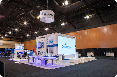 Trade show booth with white and blue displays and a large screen.