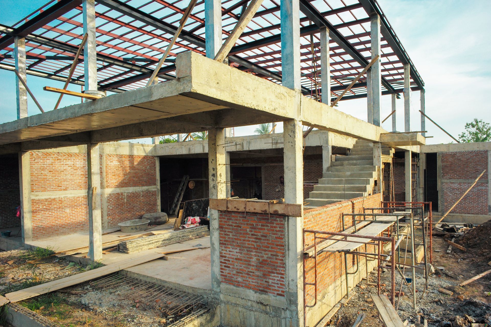 Building under construction with brick walls, concrete supports, and a steel roof framework.