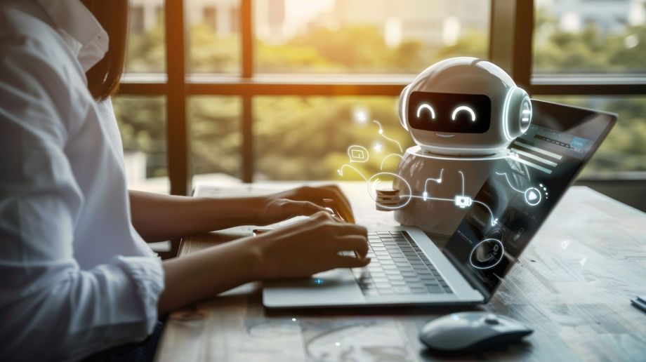 A person is typing on a laptop computer with a robot on the screen.