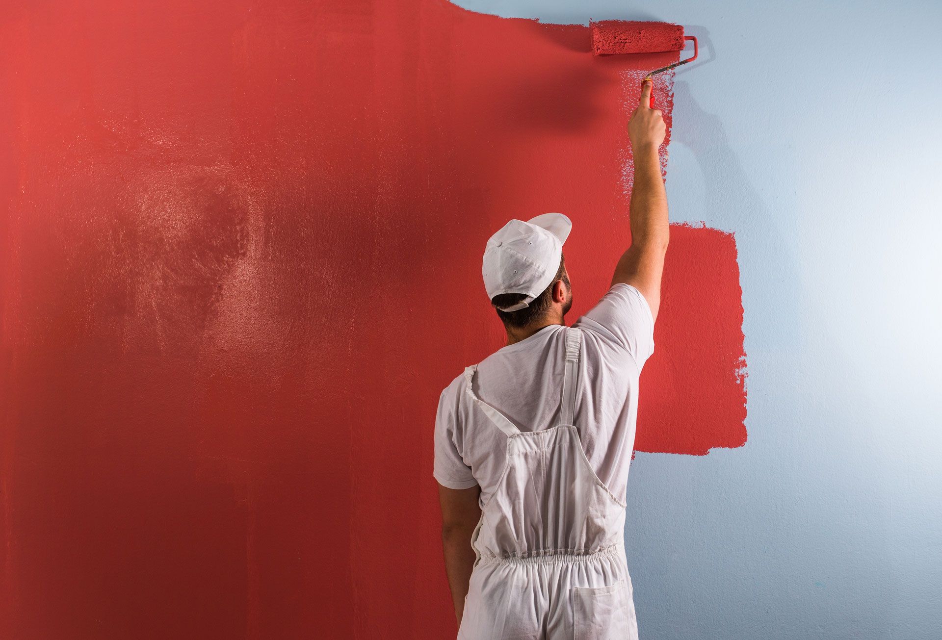 A man is painting a wall red with a roller.