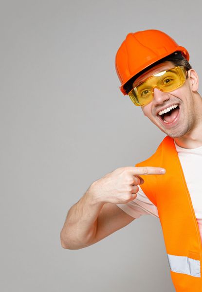 A man wearing a hard hat , safety vest and goggles is pointing at something.