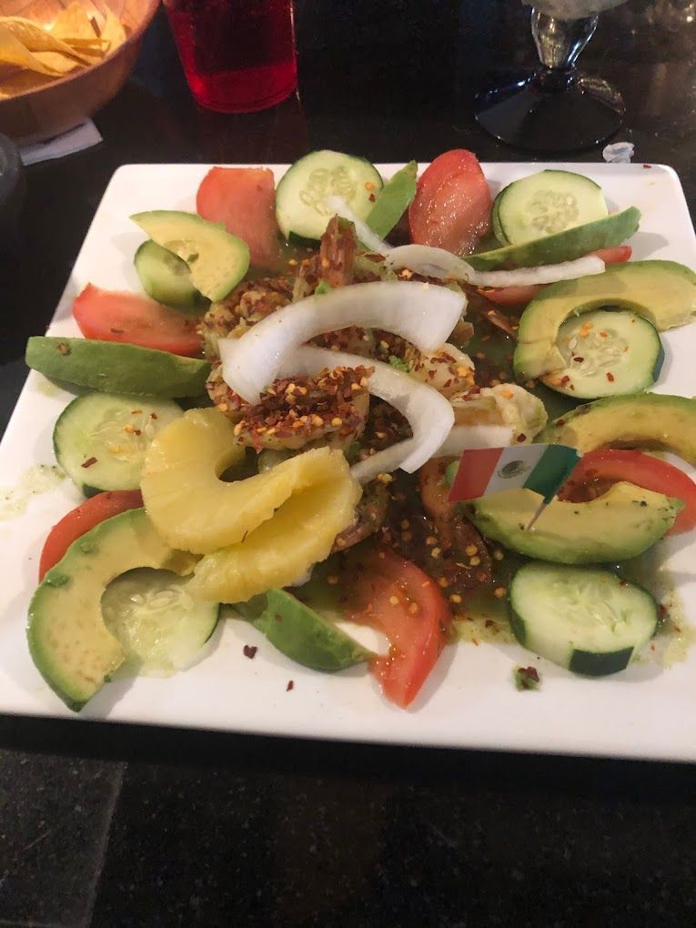A salad with avocado , tomatoes , cucumbers and pineapple on a white plate.