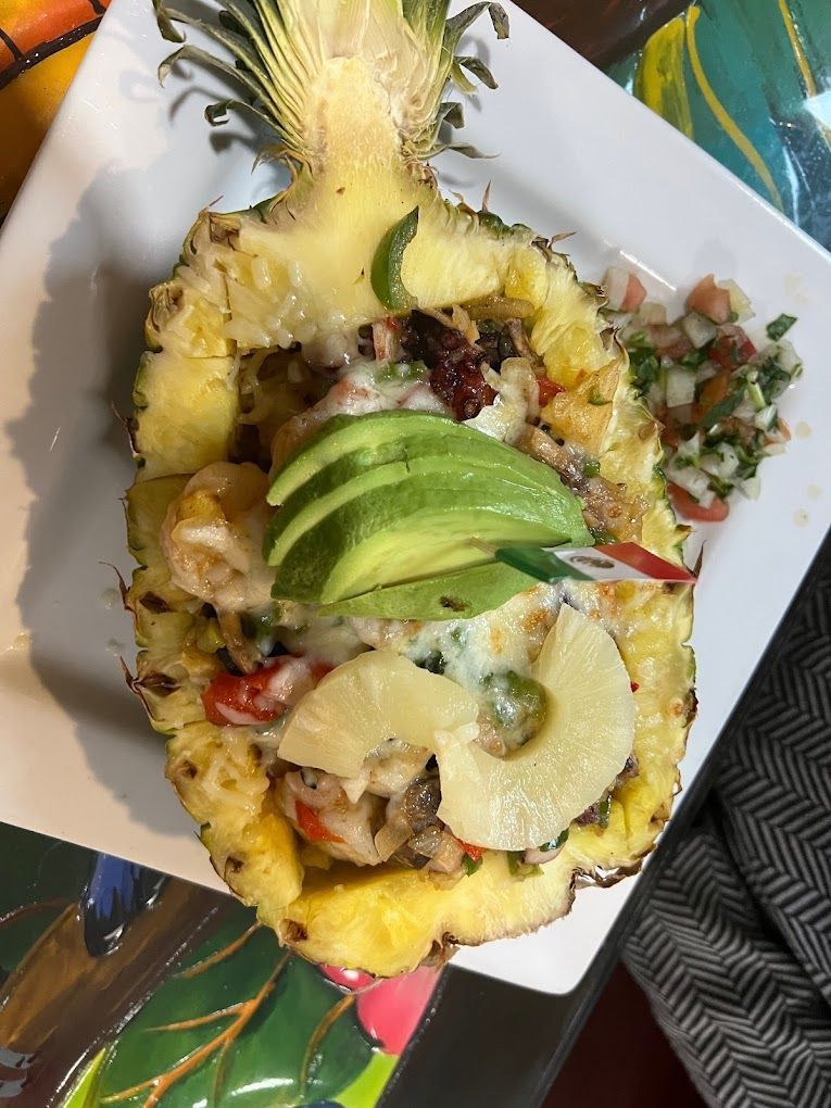 A pineapple filled with shrimp and avocado on a white plate.