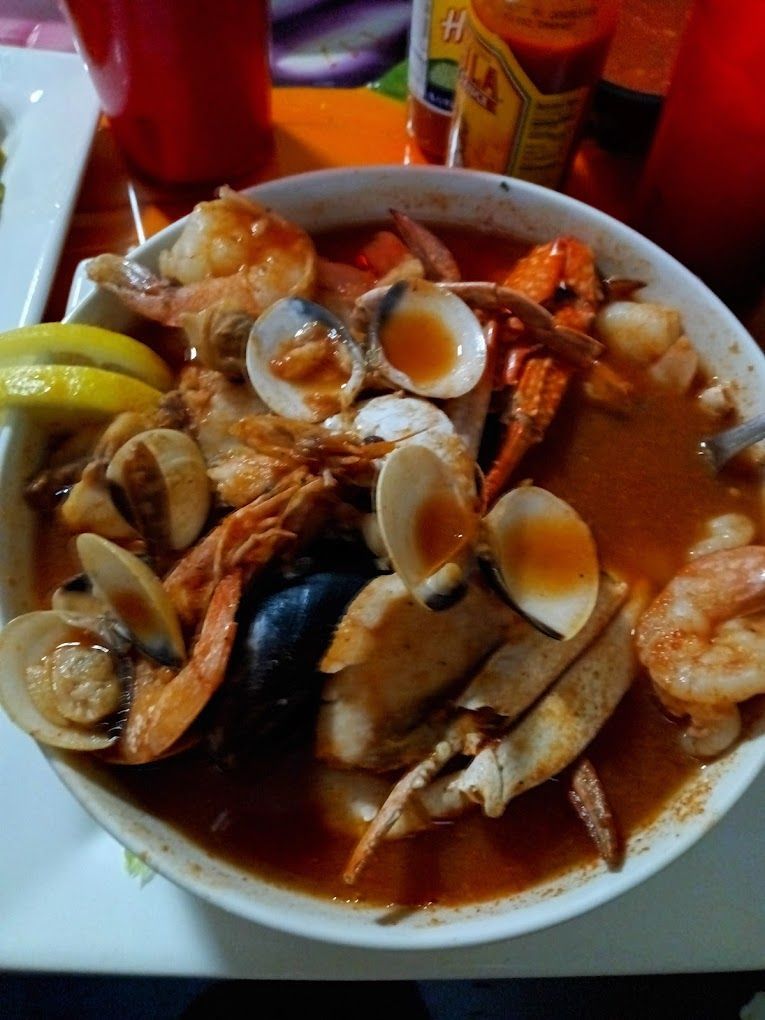 A bowl of seafood soup with a bottle of hot sauce in the background