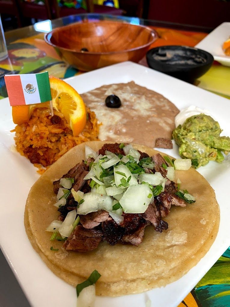 A white plate topped with a taco , beans , guacamole and an orange slice.