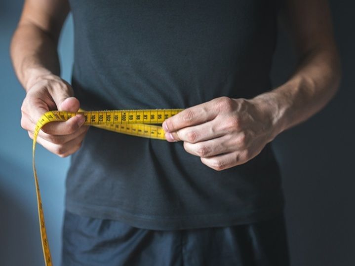 A man is measuring his waist with a yellow tape measure.