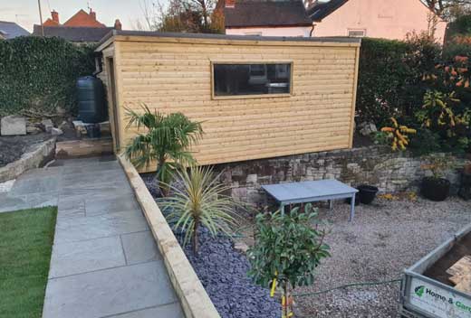 Wooden shed in a garden that's being renovated, with a pathway and