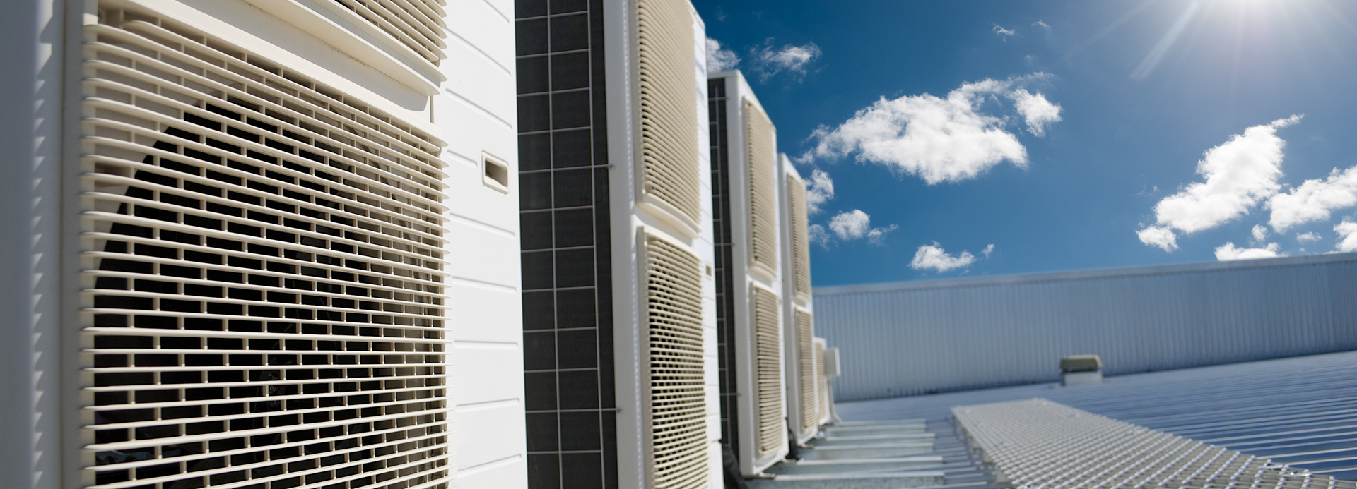 A row of air conditioners on the side of a building with a blue sky in the background.