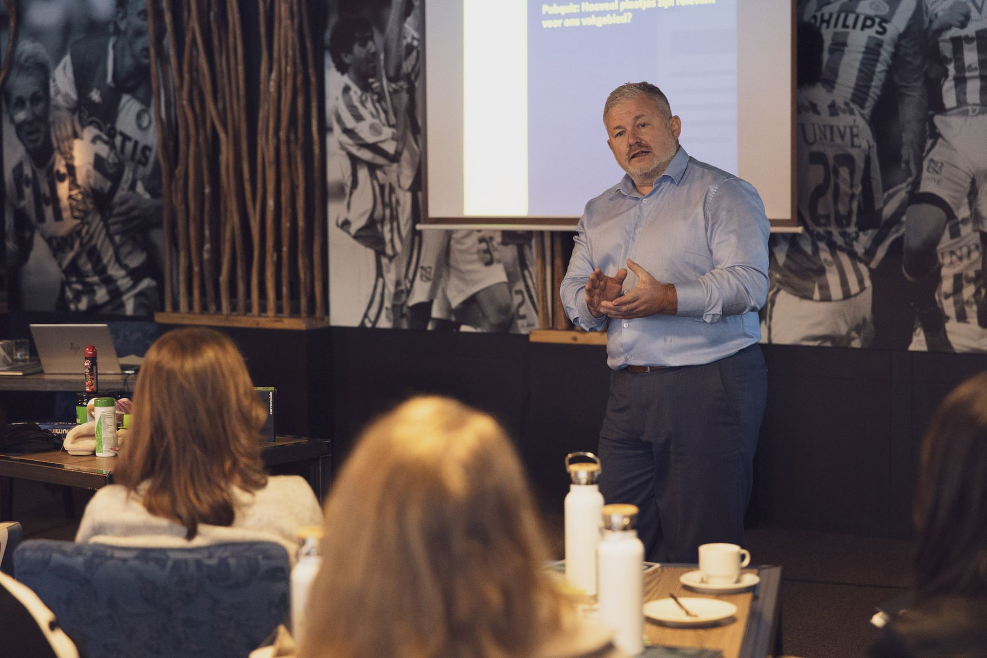 Een man geeft een presentatie aan een kleine groep met behulp van een projectiescherm in een café.