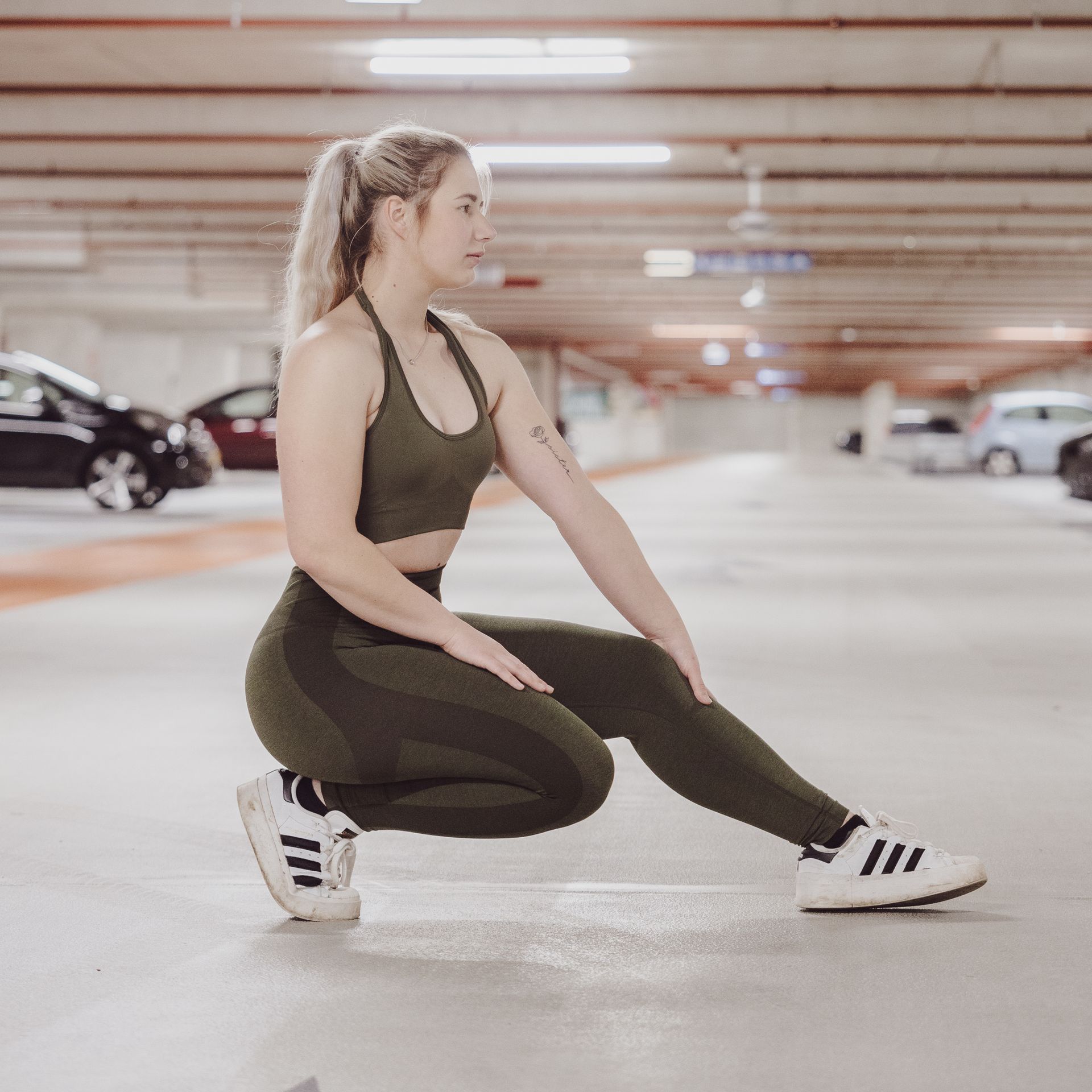 Een vrouw in olijfgroene sportkleding strekt zich uit in een parkeergarage.