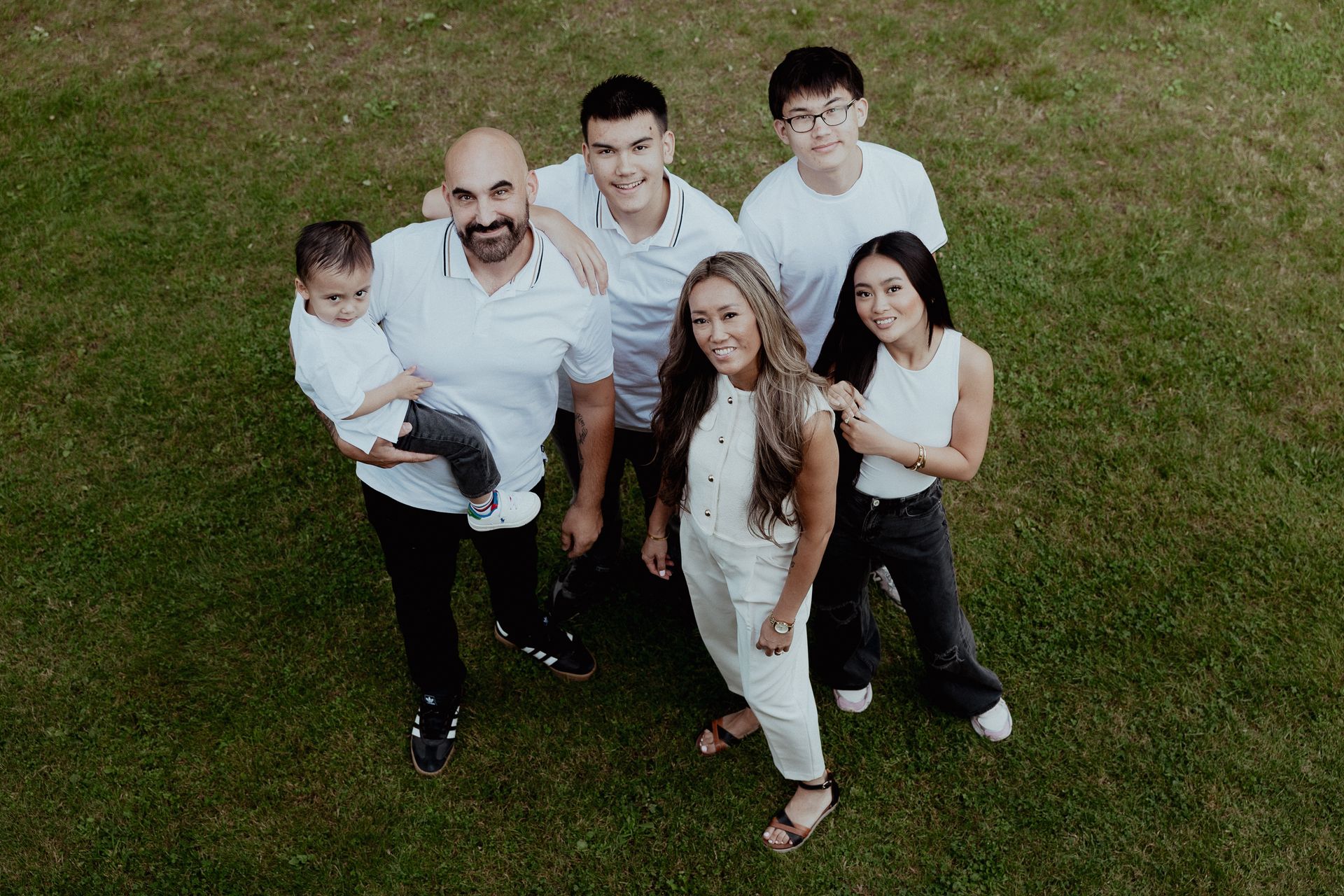 Gezin van zes staat op het gras, draagt ​​een wit shirt en lacht.