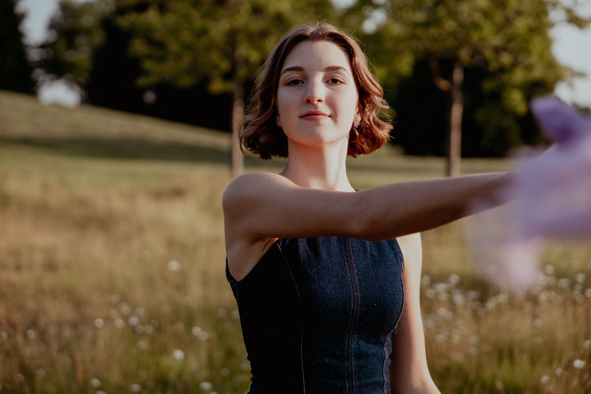 Een vrouw in een blauwe jurk zwaait met een paarse sjaal in een veld met bomen.