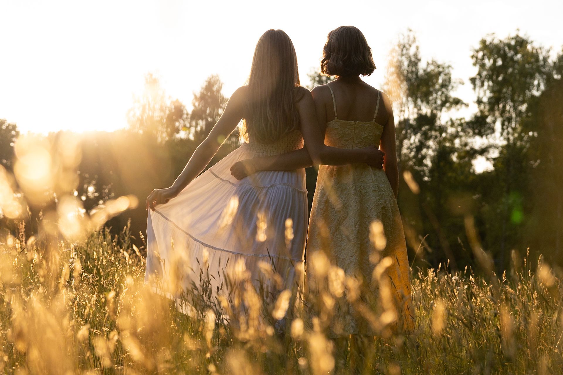Twee mensen in jurken omhelzen elkaar in een zonnig veld met hoog gras.