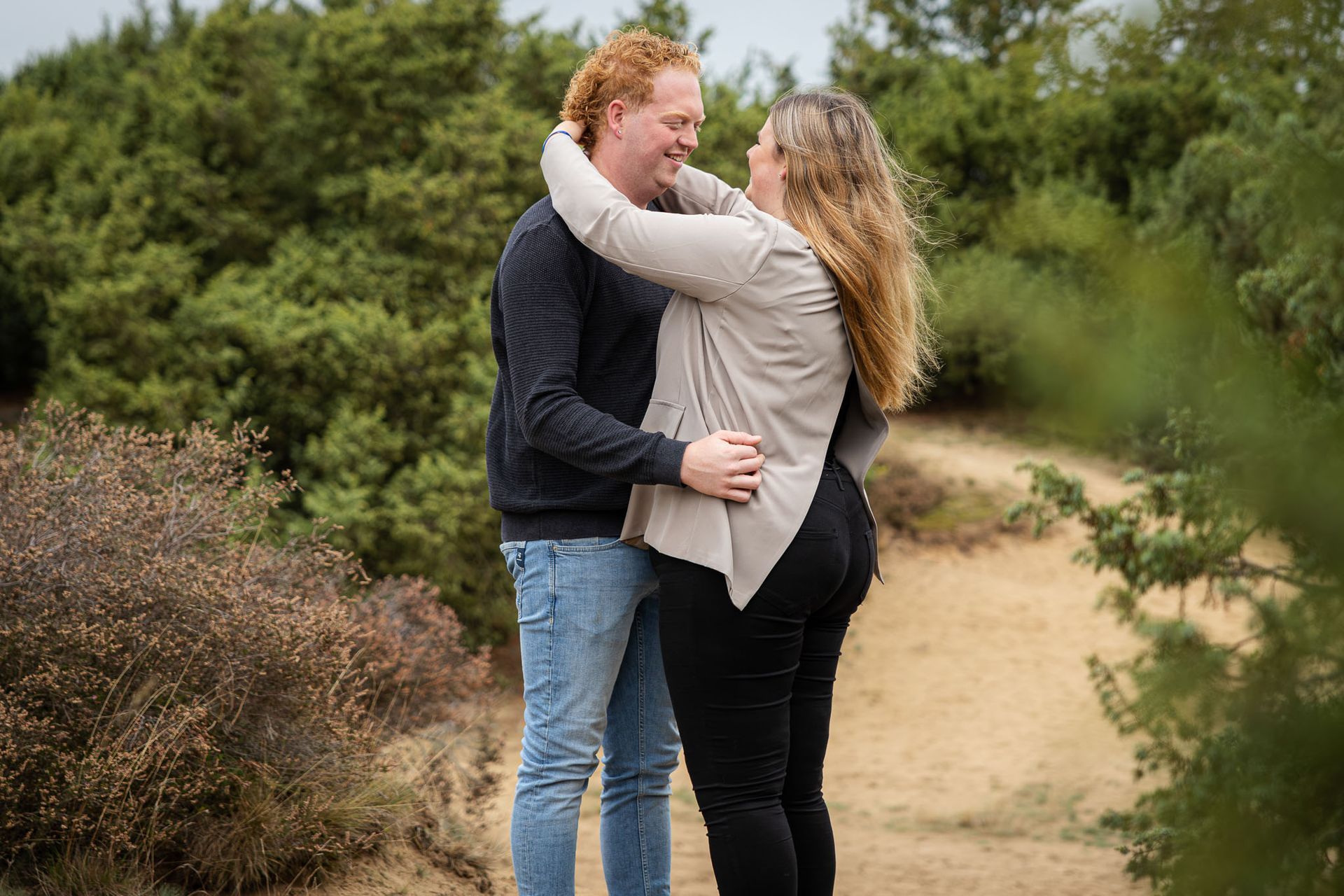 Een paar knuffelt in een natuurlijke omgeving. Een man met rood haar en een trui. Een vrouw draagt ​​een lichtgekleurd vest.