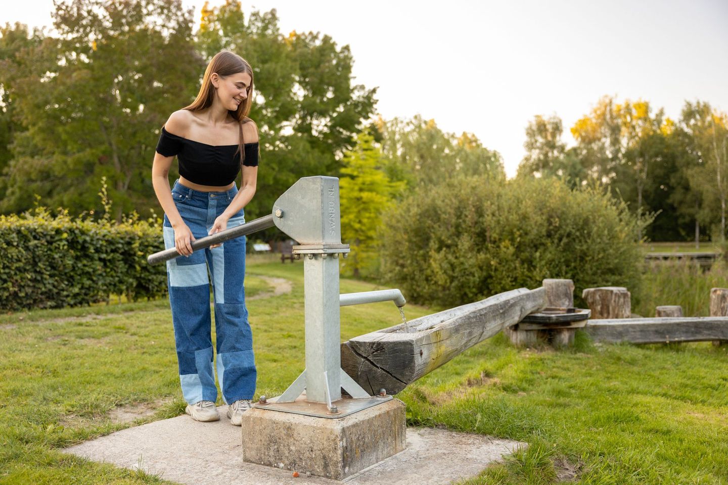 Een vrouw pompt water uit een put in een park.