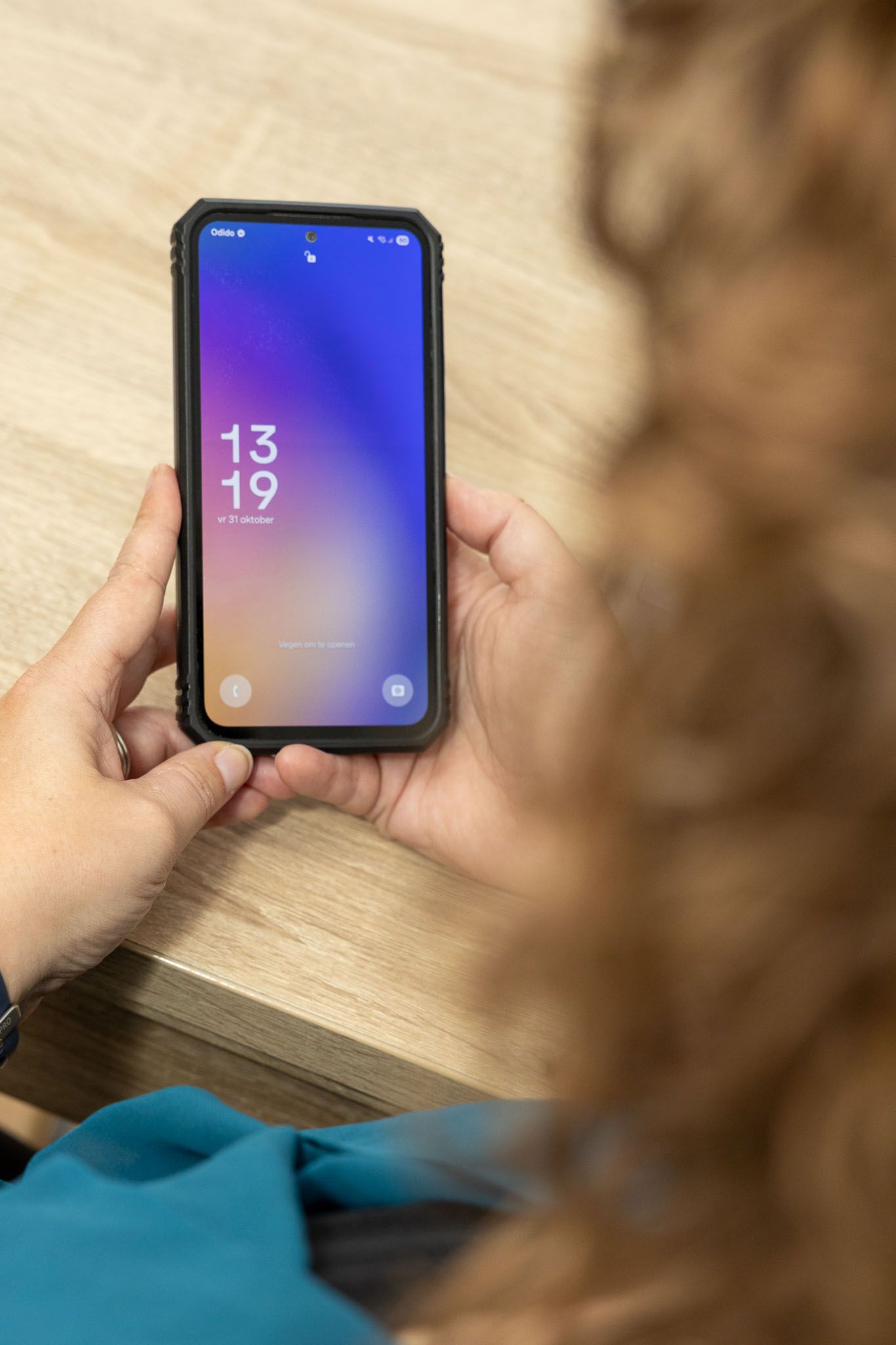 Persoon die een smartphone vasthoudt en de tijd 13:19 weergeeft op een achtergrond met een verloop van paars en blauw.