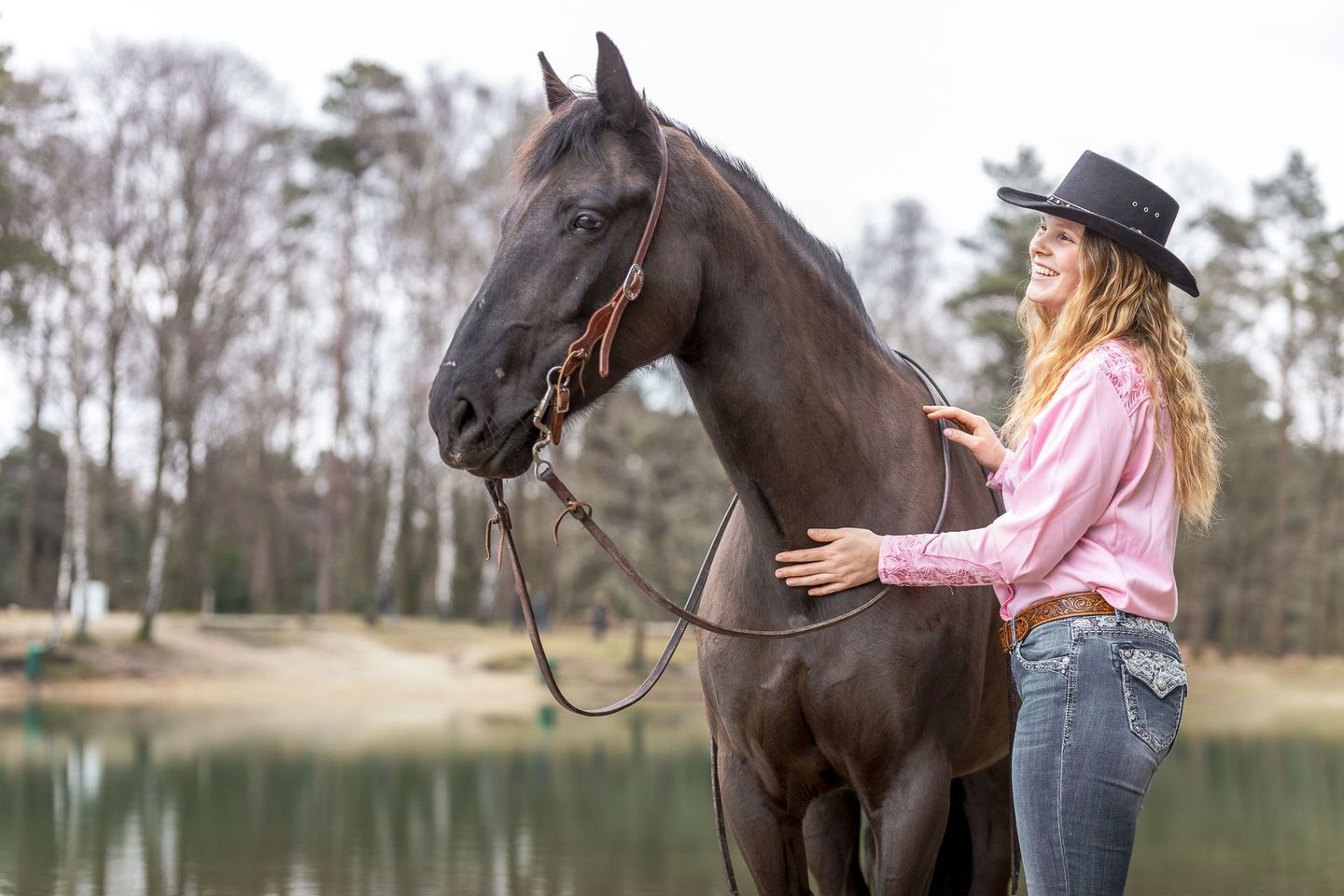 Een vrouw met een cowboyhoed staat naast een paard.