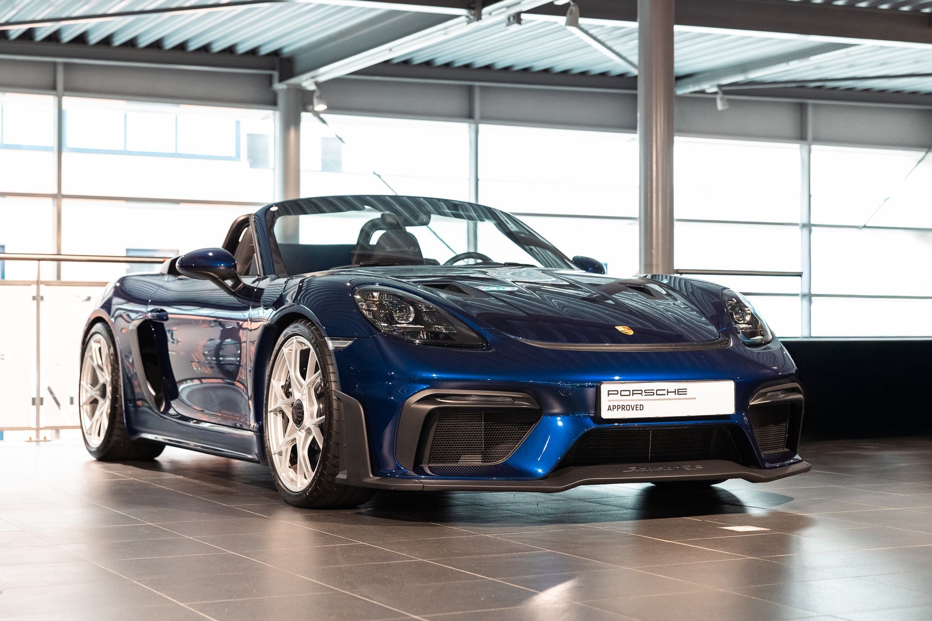 Blauwe sportwagen geparkeerd binnen onder een rasterplafond.