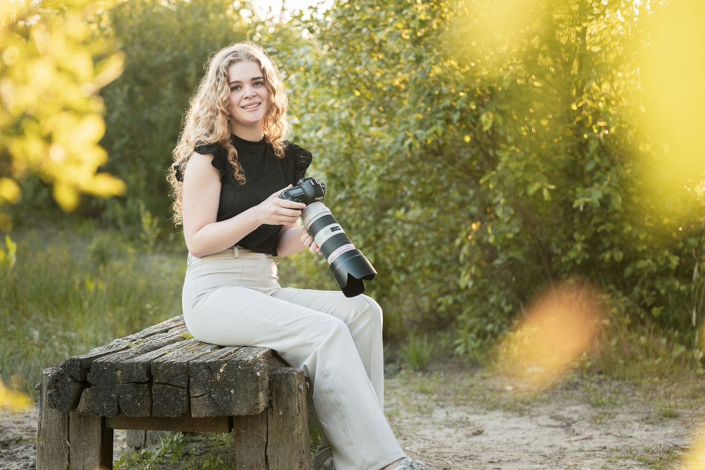 Een vrouw zit op een bankje met een camera in haar handen.
