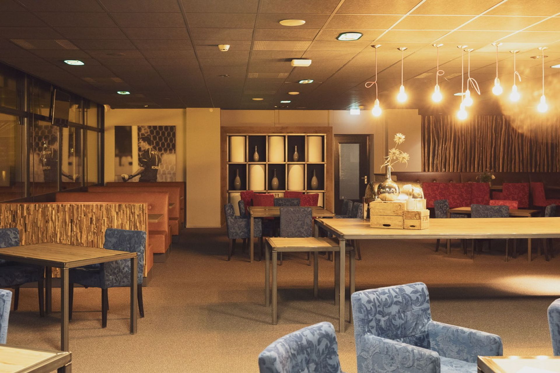 Interieur van een schemerig restaurant met tafels, banken en decoratieve verlichting.