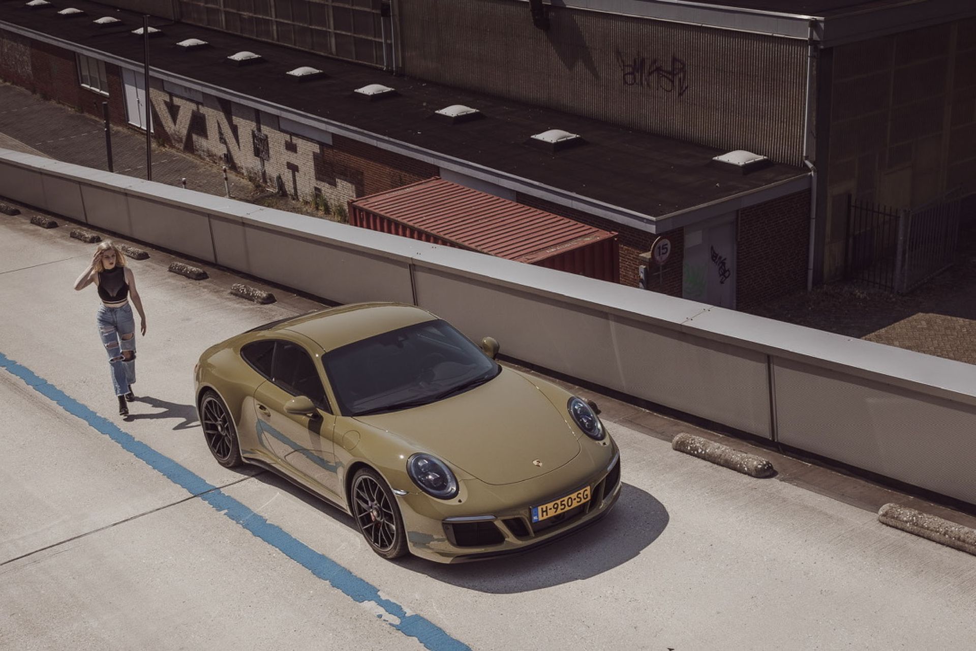 Een beige Porsche met een persoon die ernaartoe loopt, vlakbij een gebouw.