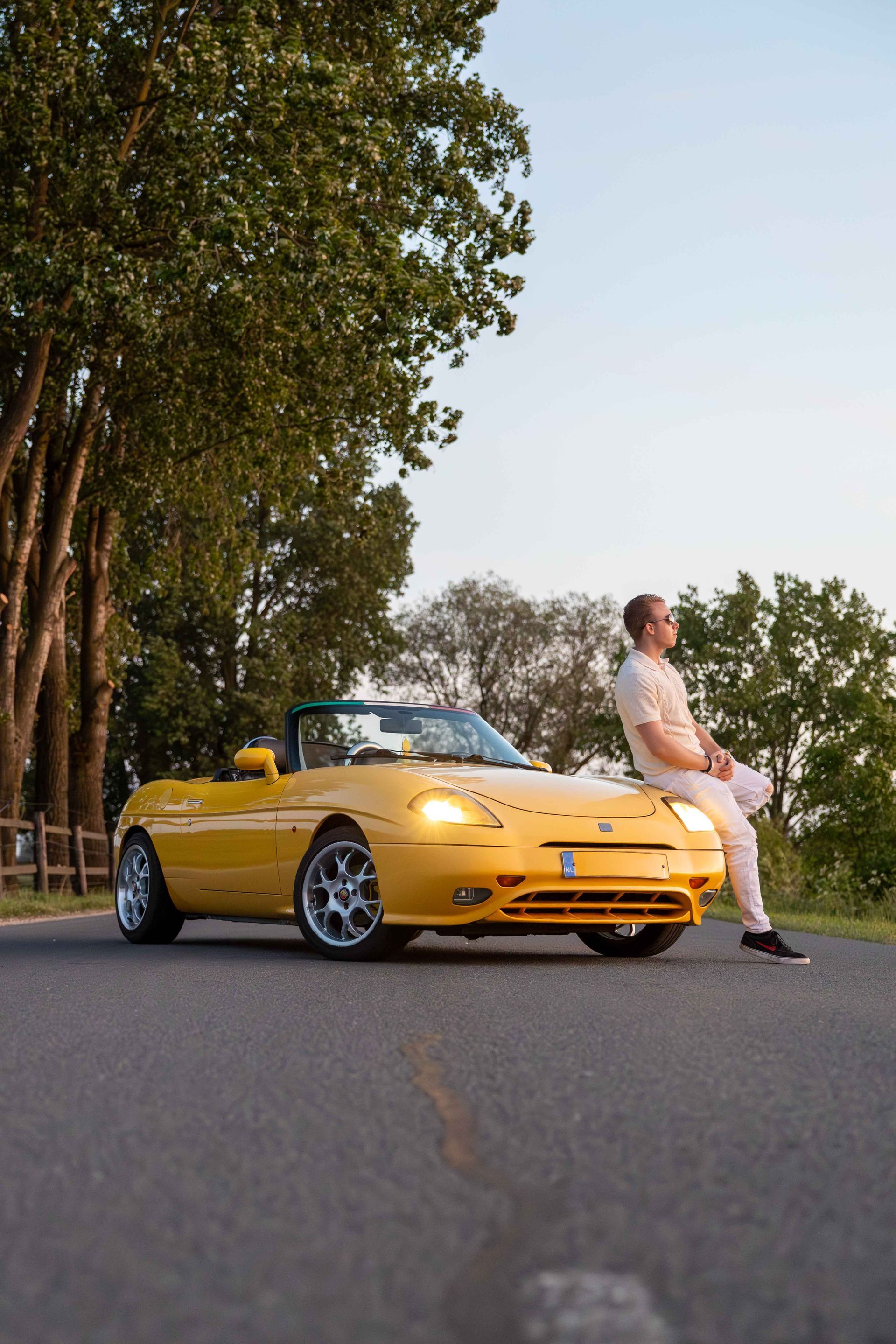 Een man zit achterop een gele sportwagen.