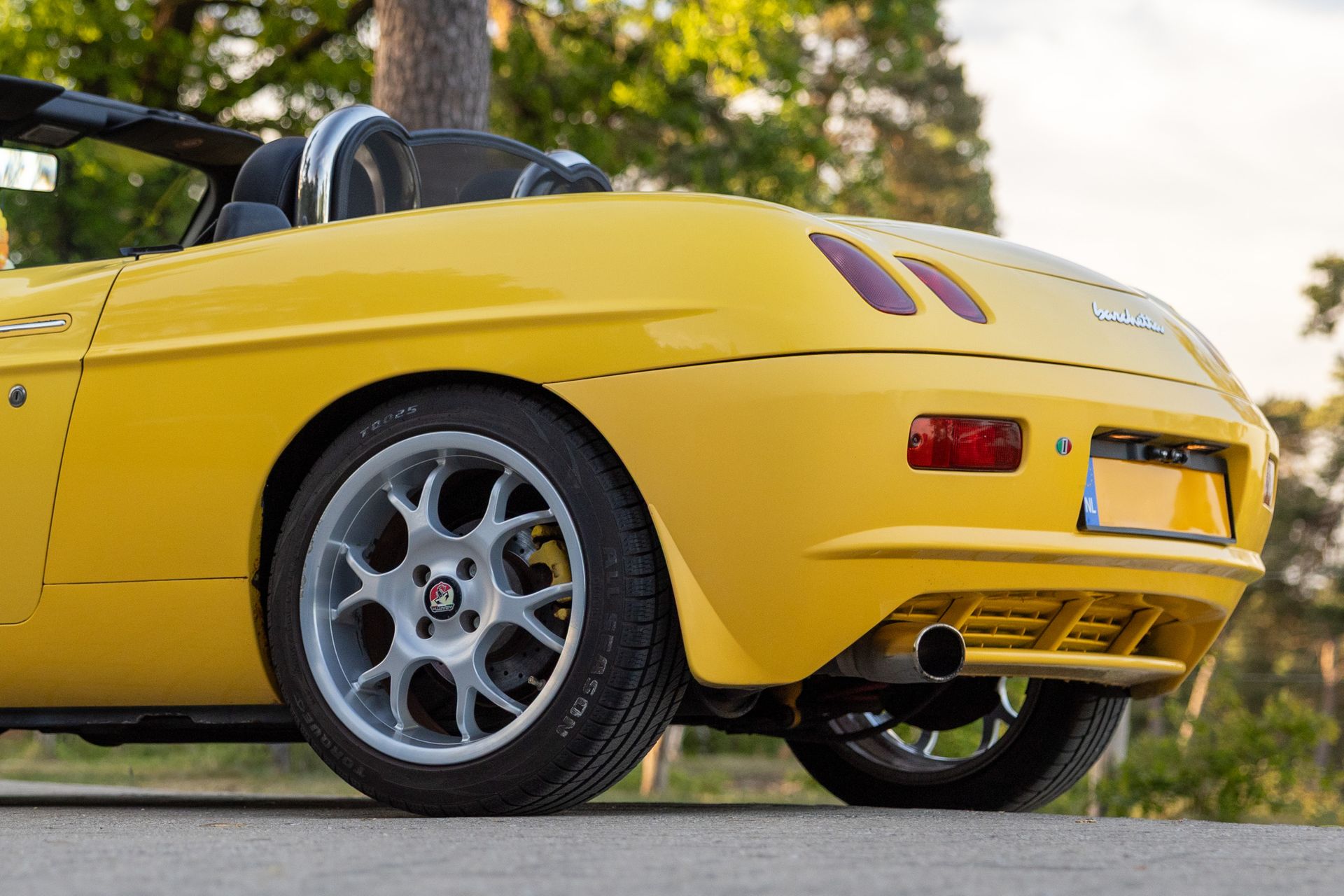 Gele sportwagen, achteraanzicht, geparkeerd in de openlucht, grijze wielen.