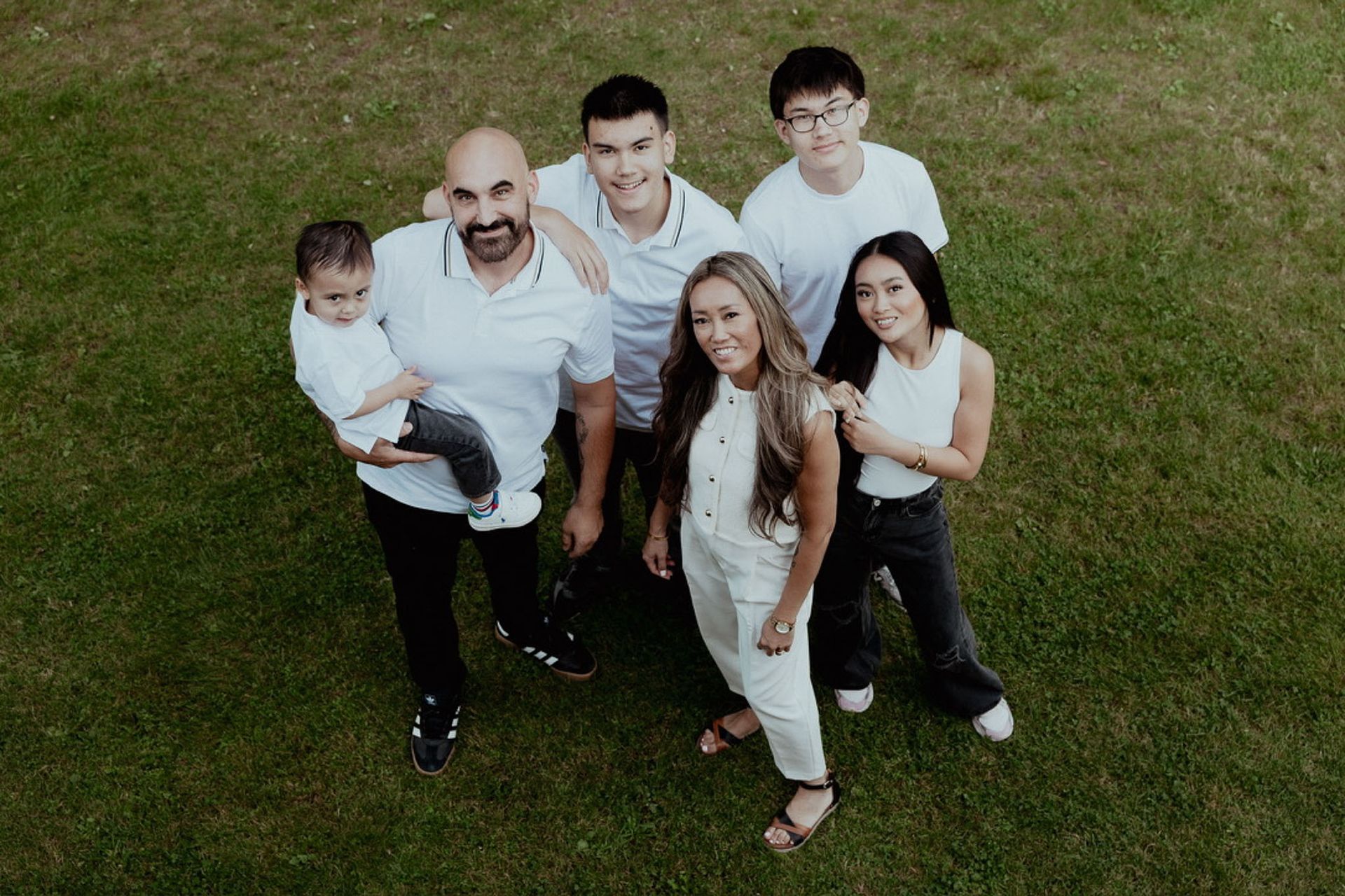 Een gezin van zes poseert op groen gras; ze dragen lichte kleding.